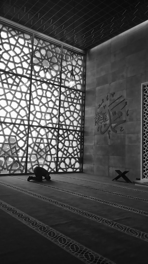 Black and white photo of a person praying inside a mosque with beautiful patterned walls in Istanbul.